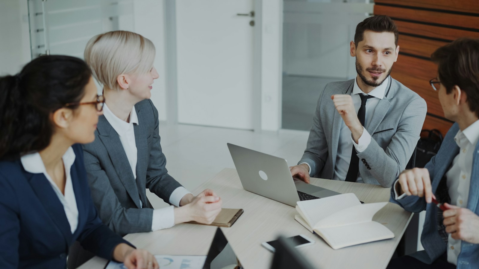 Cuatro profesionales conversan en una mesa de reuniones con una computadora portátil.